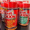 Close-up of vibrant red-capped Ragin' Cajun seasoning bottles including Ragin' Hot and Chicken & Gator flavors, featuring a fiery logo and C'EST BON text
