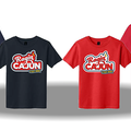 Four graphic t-shirts display the Ragin' Cajun C'est Bon! logo with a red flame and yellow text box, presented in navy blue, charcoal black, and two shades of red