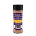 Product photography of an Acadian Kitchens spice bottle filled with brown seasoning, featuring a black flip-top lid and a vibrant purple label with white text detailing breakfast, snack, and dessert usage suggestions alongside yellow food icons on a white background