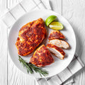 Paprika-crusted chicken breast, one whole and three sliced pieces, presented on a white plate with vibrant lime wedges and a fresh rosemary sprig on a white wooden surface