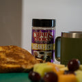 A breakfast setting featuring a purple Cajun's Choice Premium Blend Breakfast seasoning container, golden French toast, an olive green Yeti mug, and a colorful fruit salad with red grapes and melon