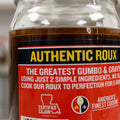 Photograph of a clear glass jar of dark brown "Authentic Roux" with a prominent red and black label featuring yellow "AUTHENTIC ROUX" text, "The Greatest Gumbo & Gravy" claim, and a "Certified Cajun" Louisiana outline logo
