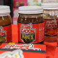 Jars of Ragin' Cajun seasonings on a red surface with blurred background