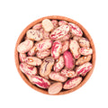 Photograph of colorful pinto beans with distinctive red and cream speckles in a rustic light brown wooden bowl on a white background