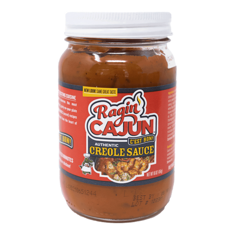 Product photography of a glass jar of Ragin' Cajun Authentic Creole Sauce featuring a vibrant red label with yellow flames, a green alligator chef mascot, an image of cooked shrimp in a skillet, and a white screw-top lid