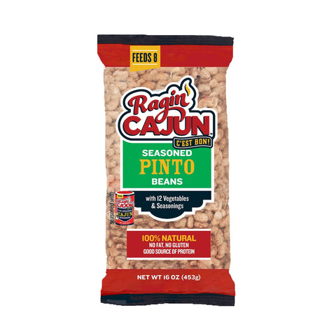 A clear plastic bag of Ragin' Cajun Seasoned Pinto Beans featuring its prominent red and white 'C'est Bon!' logo with a flame, a green label highlighting '12 Vegetables & Seasonings,' and a red banner proclaiming '100% Natural No Fat No Gluten Good Source of Protein' and 'FEEDS 8'