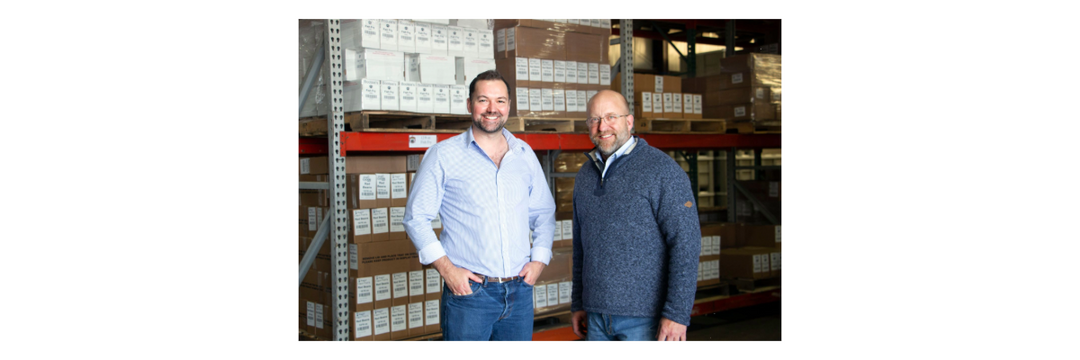 Two Acadian Kitchens team members standing in a warehouse with shelves of boxes