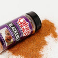 Product photography of a purple Cajun's Choice Blackened Seasoning & Rub bottle on a white surface with spilled reddish-brown seasoning and a label showing blackened meat