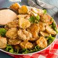 A plate of golden brown fried pickles served with creamy dipping sauce and fresh green lettuce garnish on a red and white checkered napkin