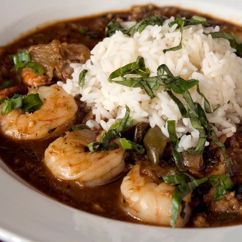 Photograph of a traditional Cajun or Creole shrimp gumbo featuring plump pink shrimp a rich dark roux and fluffy white rice garnished with vibrant green herbs