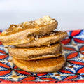 Photograph of a stack of three golden-brown pancakes drizzled with glistening syrup and topped with brown sugar, served on a vibrant blue, red, and white patterned plate