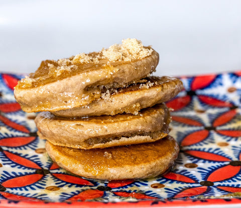 Photography a stack of three golden brown fritters glistening with syrup and sprinkled with brown sugar atop a vibrant red blue and white patterned ceramic plate