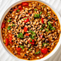 Top-down view of a flavorful black-eyed pea stew in a white bowl, featuring tender peas, bright red bell peppers, and fresh green herbs in a rich orange broth
